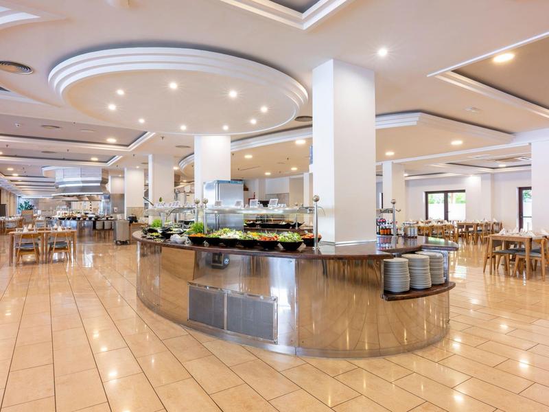 Nowoczesna, jasna jadalnia z bufetem i licznymi stołami i krzesłami.