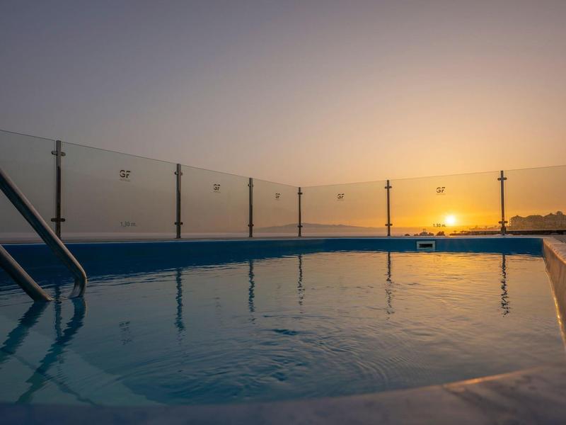 Zachód słońca nad zewnętrznym basenem z szklaną balustradą i drabinką.