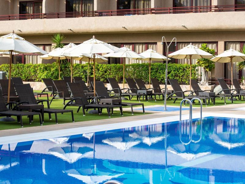 Pusta strefa basenu z leżakami i parasolami przed budynkiem hotelu