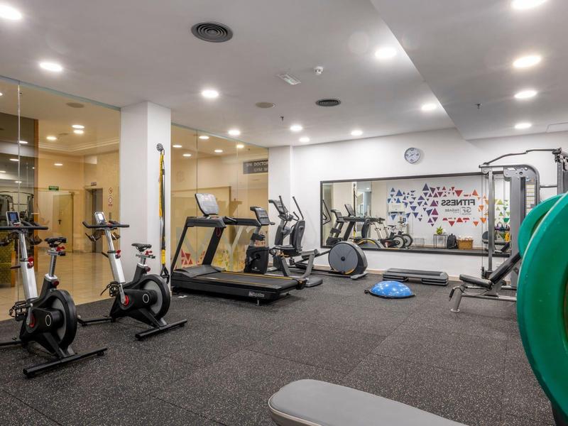 Nowoczesna siłownia z bieżniami, rowerami stacjonarnymi i ciężarami w jasnym pomieszczeniu.