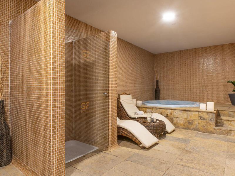 Nowoczesna strefa spa z prysznicem, leżakami i jacuzzi w ciepłych brązowych tonach.