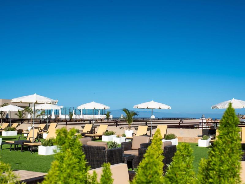 Luksusowy taras słoneczny z leżakami, białymi parasolami i widokiem na morze.