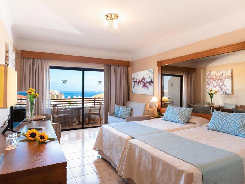 Jasny pokój hotelowy z dwoma łóżkami, balkonem i widokiem na morze.