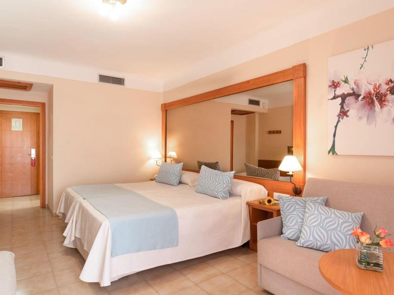 Jasny pokój hotelowy z łóżkiem podwójnym, sofą, stołem i dużymi lustrami na ścianie.