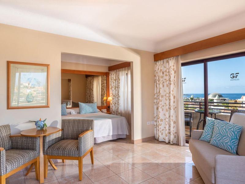 Jasny pokój hotelowy z miejscem do siedzenia, łóżkiem i balkonem z widokiem na morze.