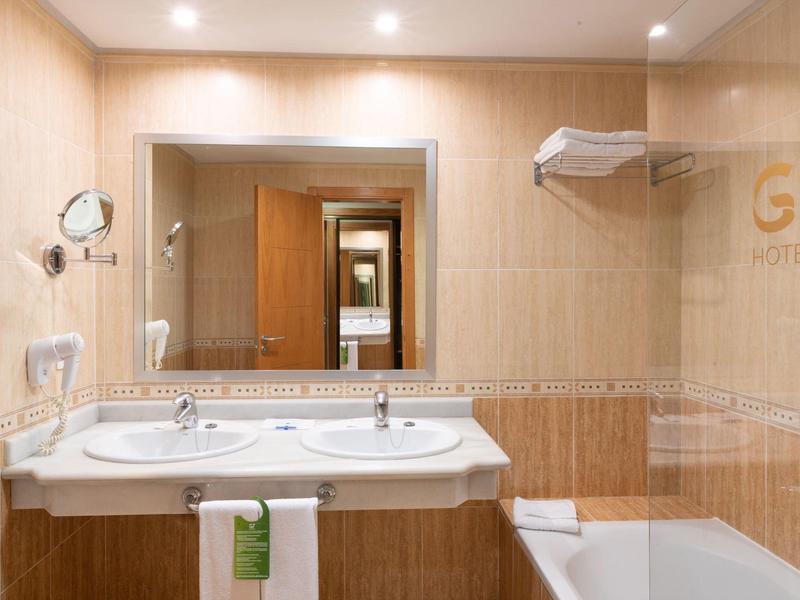 Jasna łazienka z podwójną umywalką, dużym lustrem i wanną.