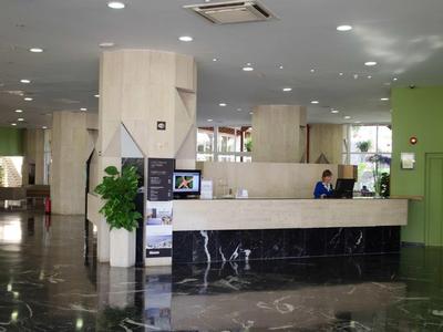 Großer Hotel- oder Büroempfang mit hellem Tresen, grünen Wänden und glänzendem Marmorfußboden.