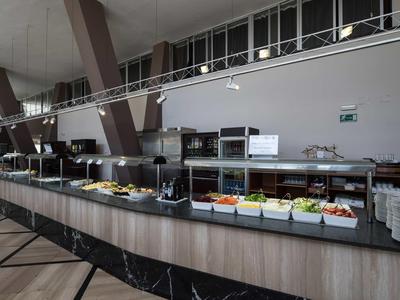 Moderne Cafeteria mit langem Buffet voller Salate, Geschirr und Küchenzeile im Hintergrund.