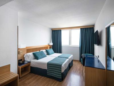 Hell eingerichtetes Hotelzimmer mit Doppelbett, blau-grünen Vorhängen und Holzmöbeln.
