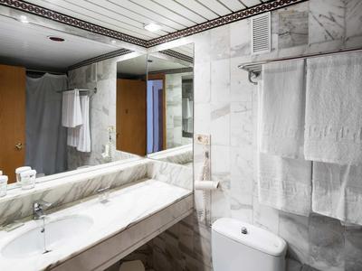 Modernes Badezimmer mit weißer Marmorverkleidung, großem Spiegel, Waschbecken und Toilette.