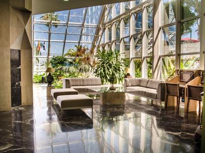 Heller Wintergarten mit großen Fenstern, Pflanzen und modernen Sitzmöbeln auf glänzendem Boden.