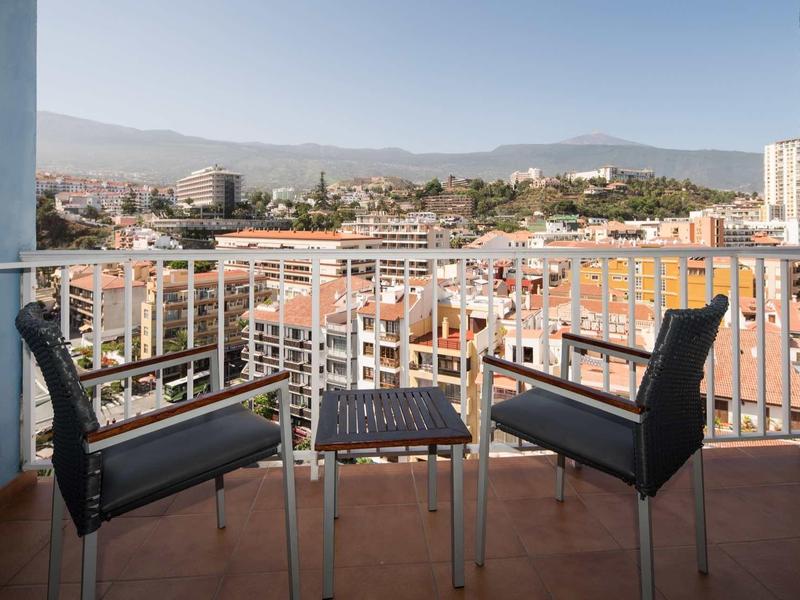 Balcon avec deux chaises et une table face à la ville et aux montagnes en arrière-plan.