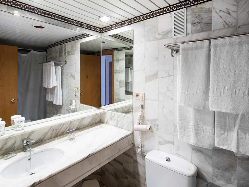 Salle de bain d'hôtel moderne avec murs en marbre, lavabo, miroir et serviettes.