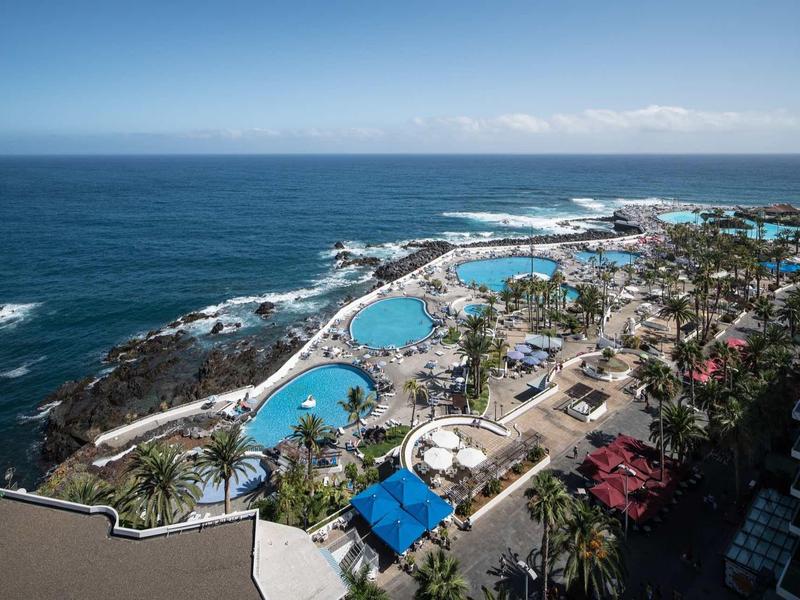Vue d'une station balnéaire côtière avec piscines, palmiers et vue sur l'océan Atlantique.