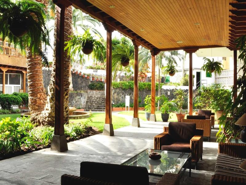 Terrasse couverte avec sièges, vue sur le jardin et la piscine dans la zone hôtelière.