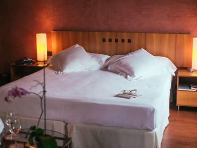 Przytulny pokój hotelowy z dużym łóżkiem, stolikami nocnymi i ciepłym oświetleniem.