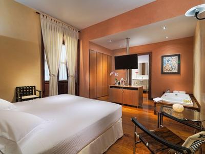 Modern eingerichtetes Hotelzimmer mit Bett, Vorhängen und angrenzendem Wohnbereich.