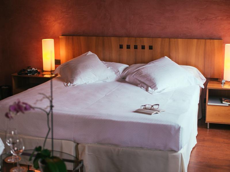 Przytulny pokój hotelowy z dużym łóżkiem, stolikami nocnymi i ciepłym oświetleniem.