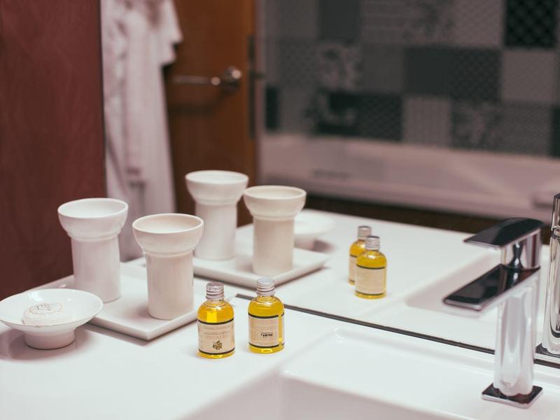 Jasna łazienka z białymi akcesoriami, małymi buteleczkami i lustrem.