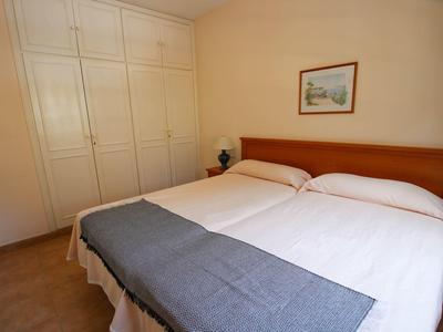Schlichtes Schlafzimmer mit Doppelbett, weißen Wänden, eingebautem Schrank und kleinem Nachttisch.