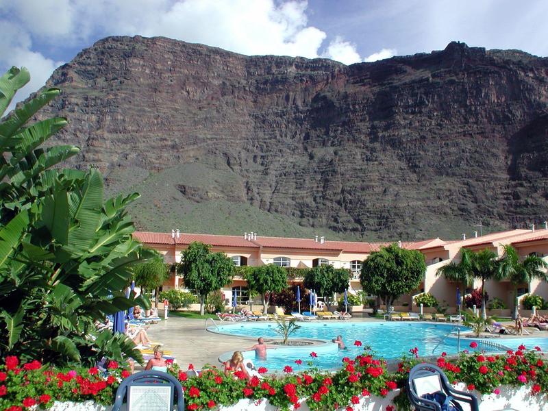 Complexe hôtelier avec piscine devant une falaise escarpée et ciel nuageux