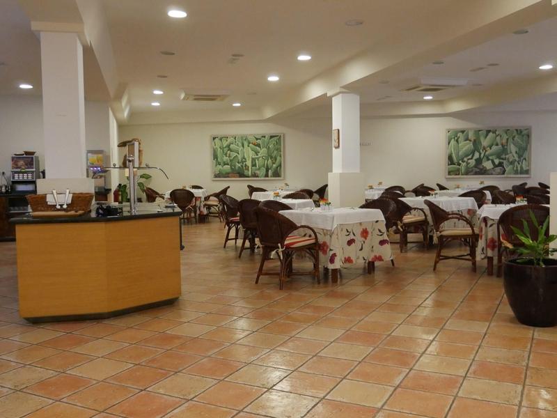 Salle de petit-déjeuner lumineuse avec rangées de tables, buffet, plante en pot et tableaux muraux.