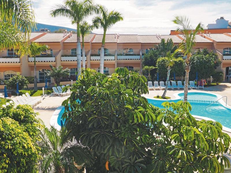 Complexe hôtelier avec grandes piscines, palmiers et végétation tropicale sous ciel clair.