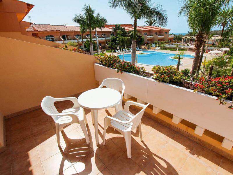 Balcon avec table et chaises blanches, vue sur une piscine et des plantes tropicales.