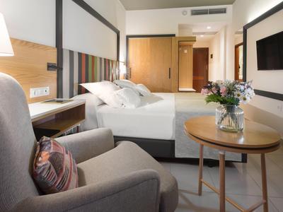 Modern hotel room with comfortable bed, armchair, table, and wall-mounted TV.