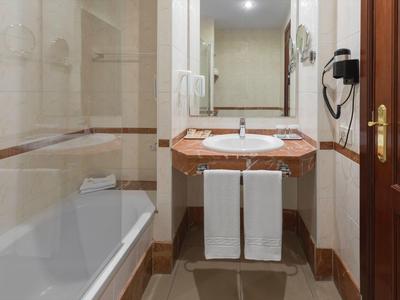 Compact hotel bathroom with bathtub, sink, and wooden door.