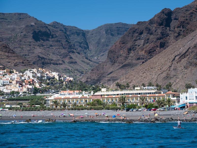 Beach and hotel buildings set against a mountainous landscape under clear skies.