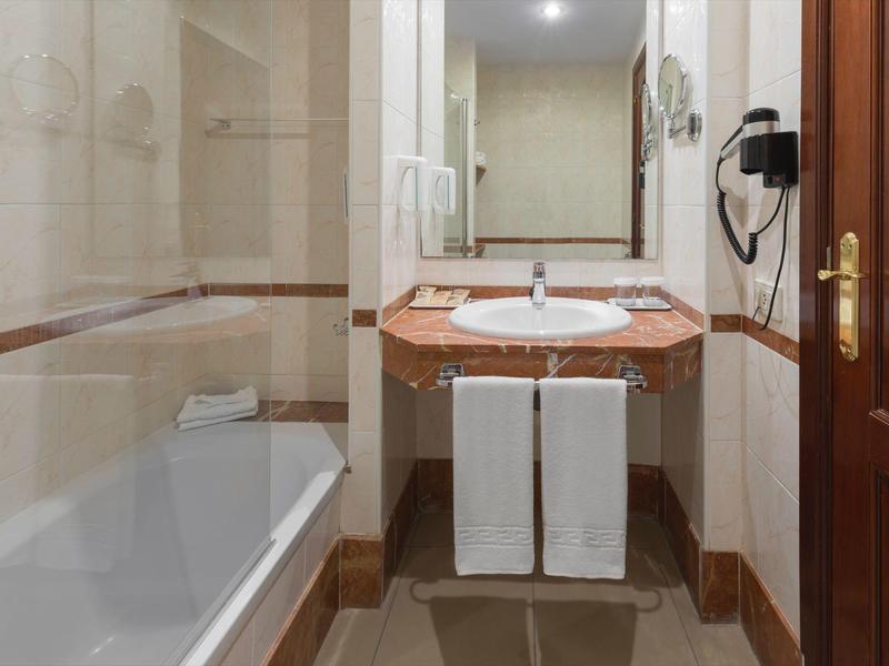 Compact hotel bathroom with bathtub, sink, and wooden door.