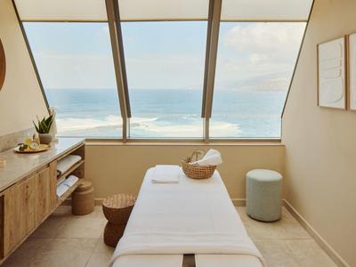 Helles Massageraum mit Blick aufs Meer, Liege, Holzschrank und minimalistischer Dekoration.