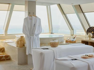 Heller Wellnessraum mit Jacuzzi, Liegen mit weißen Tüchern und Bademantel an großem Fenster.