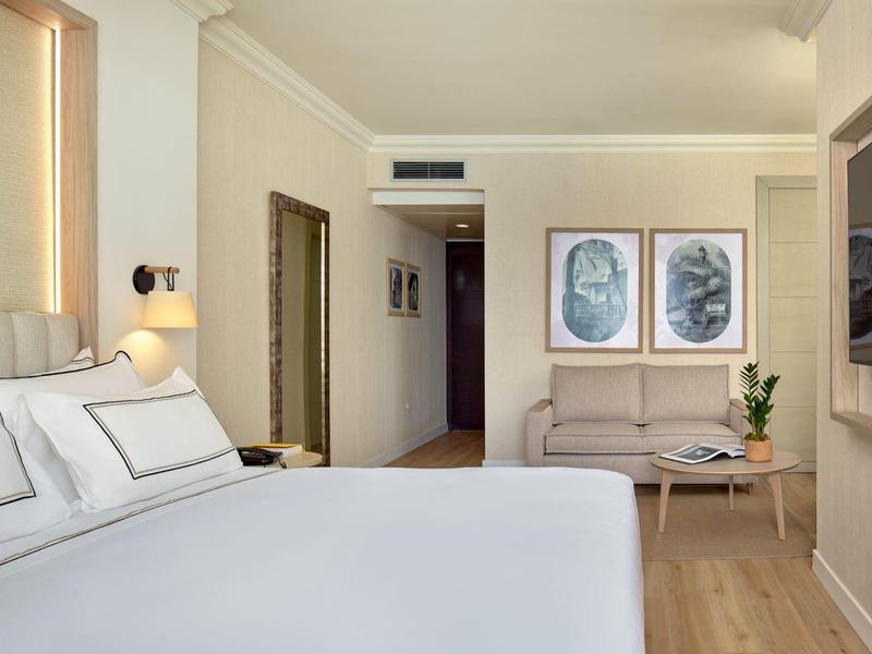 Moderne hotelkamer met groot wit bed, houten vloer en minimalistische inrichting.