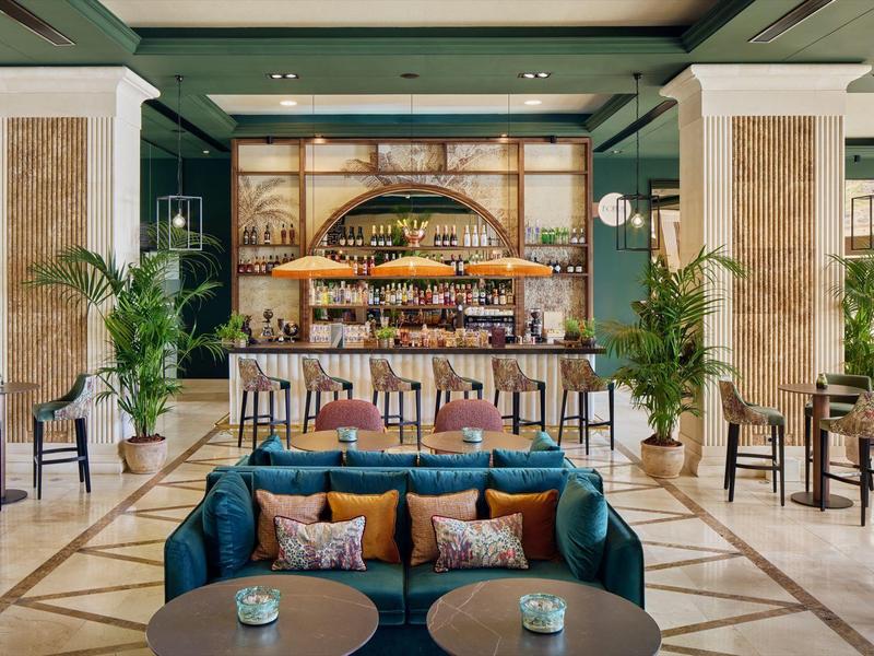 Elegante hotellounge met houten bar, gezellige zitplaatsen, groene muren en planten binnen.