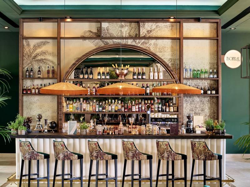 Stijlvolle hotelbar met houten schappen, diverse flessen en zes patroonrijke barkrukken onder warme verlichting.