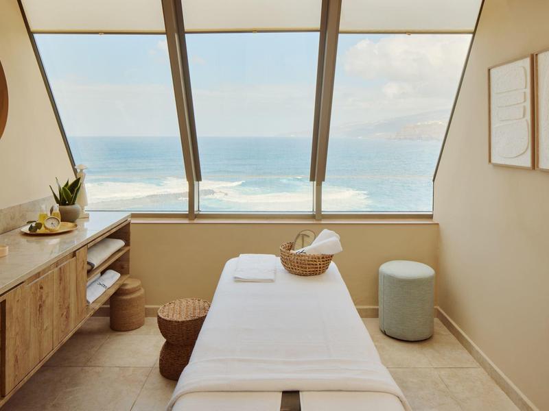 Rustige spakamer met massagetafel en uitzicht op zee door grote ramen.