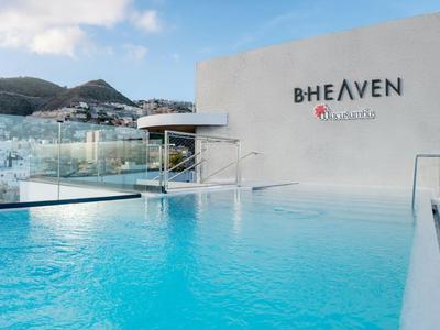 Moderner Infinity-Pool mit Blick auf eine Stadt und Berge an einem sonnigen Tag.