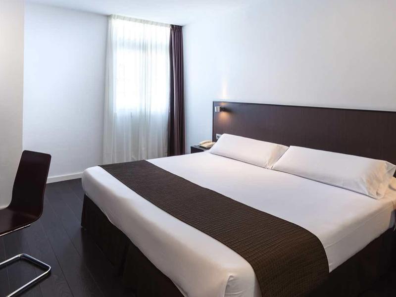 Habitación de hotel moderna con cama doble, escritorio y silla a la luz del día.