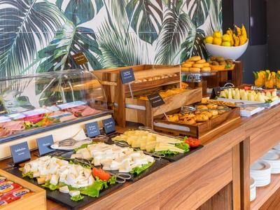 Buffet avec pâtisseries fraîches, fruits et charcuterie dans un cadre hôtelier moderne.