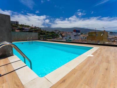 Modern rooftop pool with clear water and city view under a blue sky.