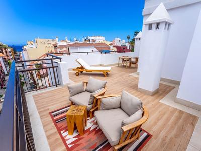 Terrasse sur le toit avec fauteuils confortables, chaises longues et table en bois sous un ciel bleu vif.