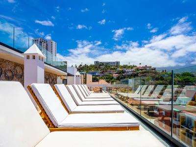 Row of white sun loungers on a sunny hotel rooftop overlooking the city and blue sky.