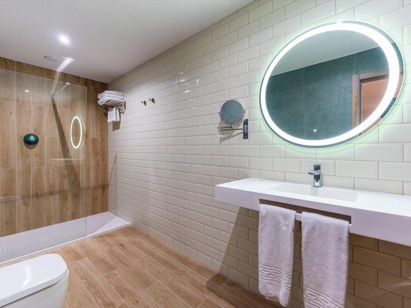 Salle de bain moderne avec miroir éclairé, lavabo, baignoire et sol en bois.