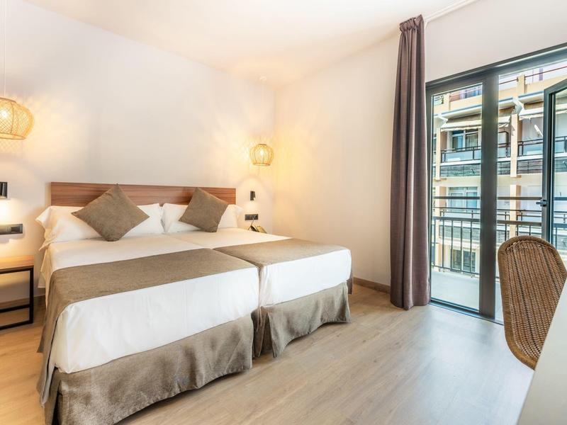 Chambre d'hôtel lumineuse avec deux lits simples, balcon et design moderne.