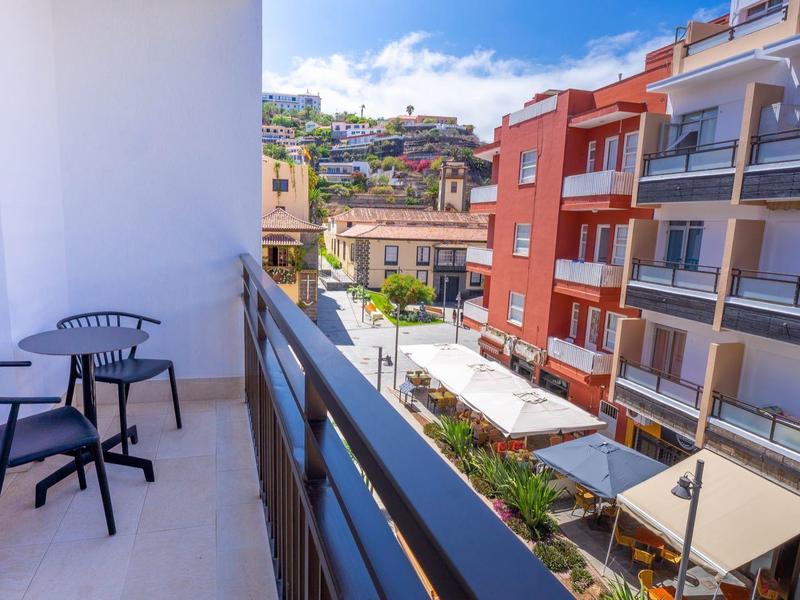 Balcon avec deux chaises et une table donnant sur des bâtiments voisins par une journée ensoleillée.