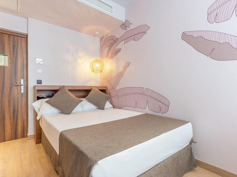 Chambre d'hôtel compacte avec lit double, deux oreillers et décor mural neutre.