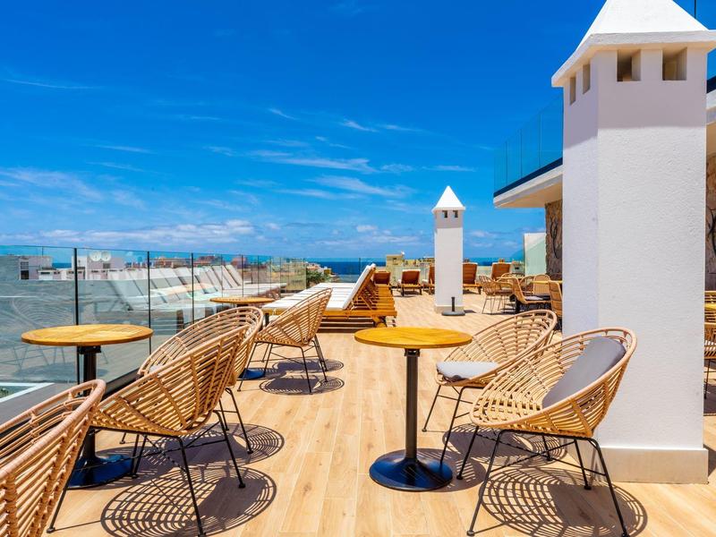 Terrasse avec des chaises et tables modernes avec vue sur la mer sous un ciel bleu.
