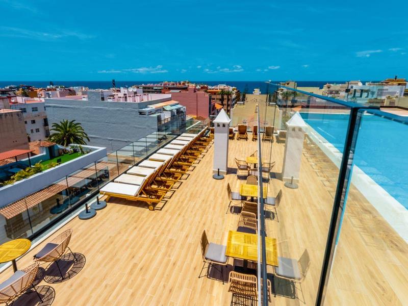 Grande terrasse en bois avec tables et chaises, garde-corps en verre et vue sur la mer.
